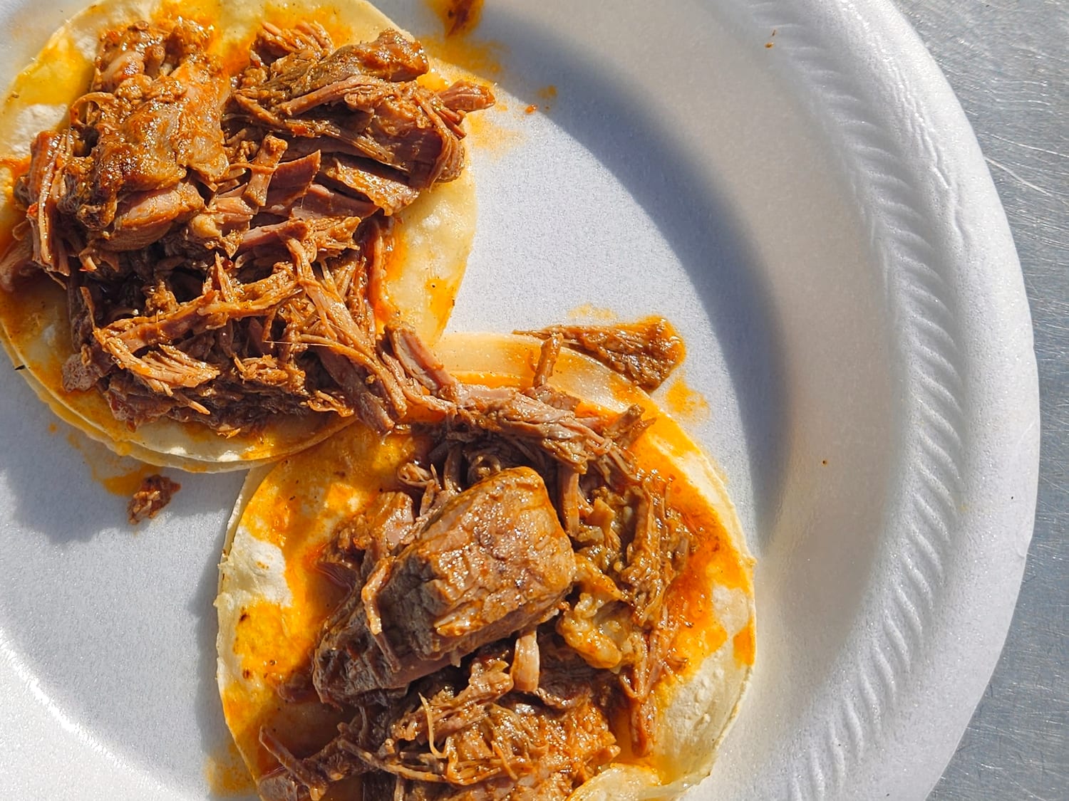 Two barbacoa tacos on corn tortillas at the truck window